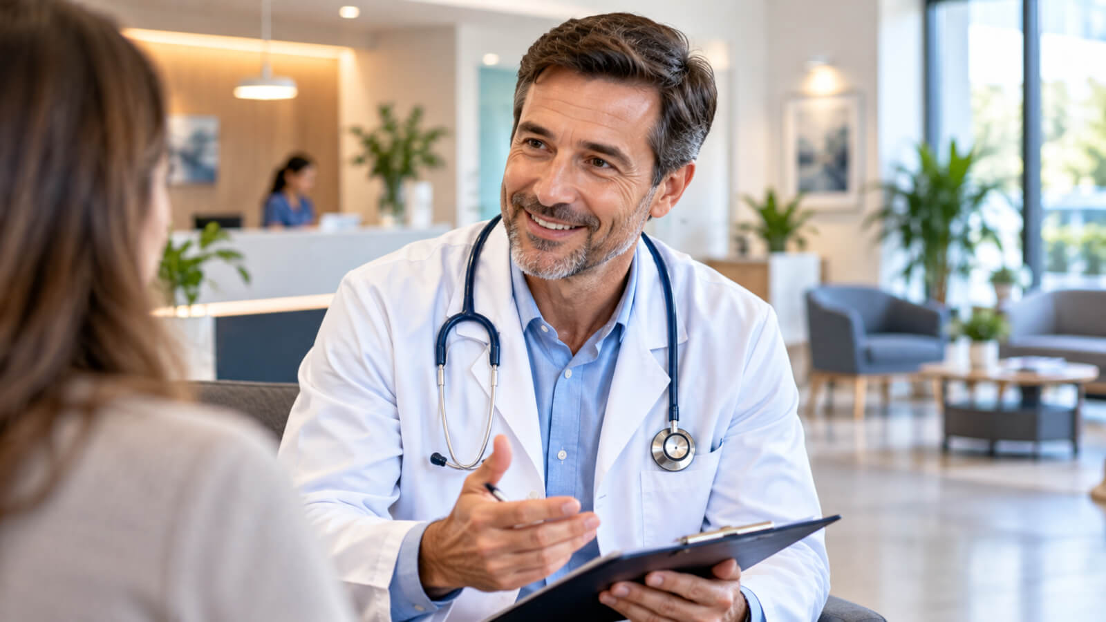 Médico con estetoscopio conversa con una paciente en una sala luminosa.